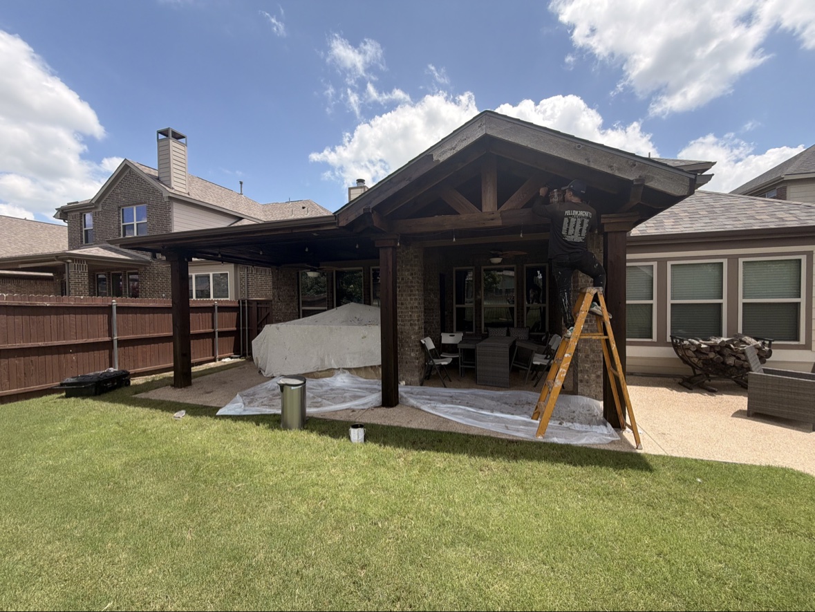 Worker staining wooden patio cover frame, outdoor structure builders Dallas TX